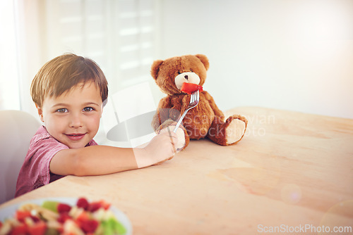 Image of Child, portrait and feeding fruit to teddy bear with fantasy play, imagination and watermelon for nutrition in dining room. Boy, kid and stuffed animal with breakfast bowl at lounge table for sharing
