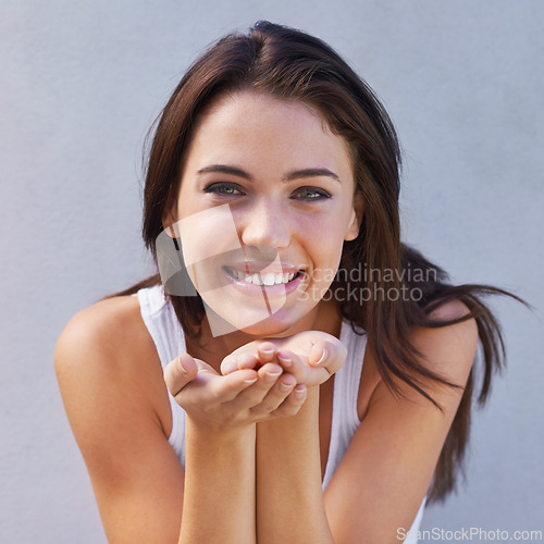 Image of Portrait, smile and blowing kiss with woman on gray wall background for flirting, love or romance. Face, affection and emoji hand gesture with happy young person looking satisfied on valentines day