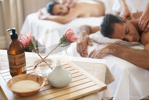 Image of Hotel, flowers and couple in spa to relax on bed or break with luxury pamper treatment tools on table. Protea, facial oil or woman with man at resort or salon for natural healing benefits or massage