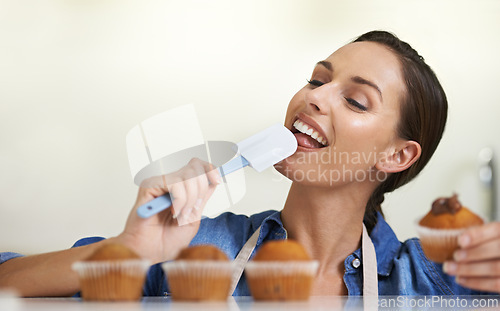 Image of Baking, cupcakes and woman with spatula in kitchen tasting sweet chocolate frosting for dessert. Cooking, eating and young female baker working on muffins and licking tool at home or apartment.