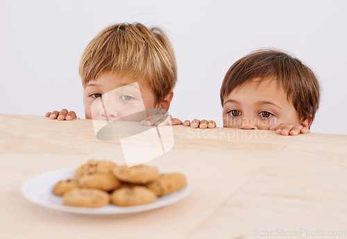 Image of Children, table and peeking at cookies for curiosity, observation and sneaking with glance. Anticipation, wonder and kids by desk with biscuits for hunger, hiding and playful brothers at home