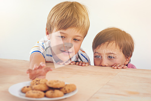 Image of Kids, boys and smile for cookies in home with stealing, peeking and childhood fun in at dining room table. Siblings, children and happy for biscuits, snack and baked goods in kitchen of apartment