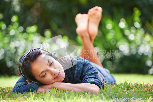 Image of Grass, park and woman with headphones, listening to music and streaming audio with peace, relaxing or summer. Person in a garden, outdoor or girl with headset or podcast with radio, sunshine or sound