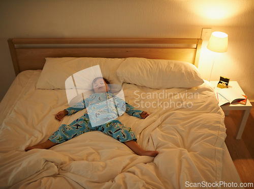 Image of Boy, bed and rest for night, sleeping and tired with fatigue and peace. Child, dreaming and exhausted with pyjamas, dark and bedroom with lamp for serene childhood at home or house for calm kid