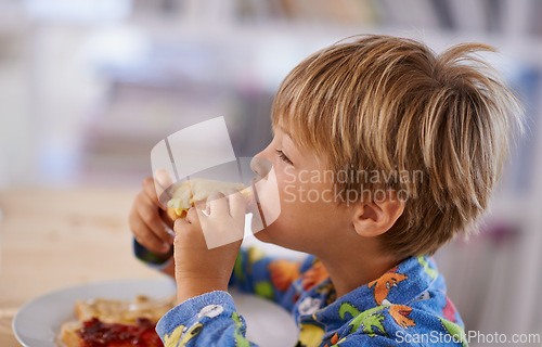 Image of Food, breakfast and boy eating a sandwich in morning, pyjamas and home for nutrition. Children, hungry and meal for young male for lunch, childhood development and bread for health and wellness