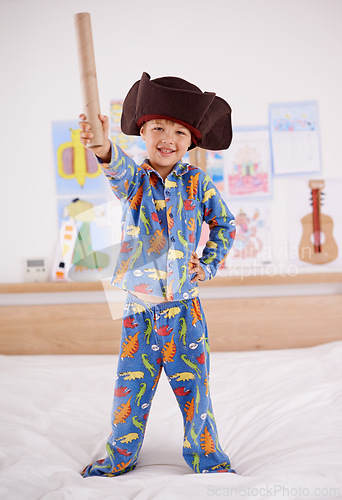 Image of Child, portrait and happy for pirate game, character and creativity in bedroom or at home. An excited boy or kid on a bed with cardboard, cap and pajamas for fun holiday, imagination and play alone