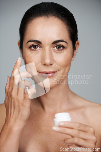 Image of Portrait, woman and apply cream for skincare in studio isolated on a gray background. Face, cosmetics and mature model with moisturizer in container for dermatology, beauty or hydration for antiaging