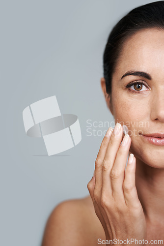 Image of Portrait, beauty and lotion with mature woman in studio on gray background for hydration or wellness. Half face, skincare or cream and serious model with moisturizer in hand to apply for antiaging