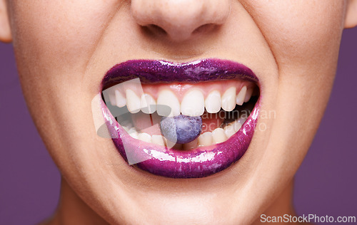 Image of Beauty, lipstick and woman with blueberry in mouth, organic makeup and creativity with shiny cosmetic product. Vegan, eco friendly and purple lip gloss for aesthetic with fruit on studio background