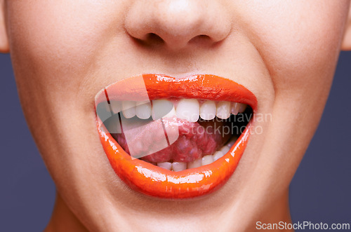 Image of Beauty, lipstick and woman with tongue out, makeup and closeup of shiny cosmetic product with skin. Lick, flirting and orange lip gloss for aesthetic in studio with cosmetology on blue background