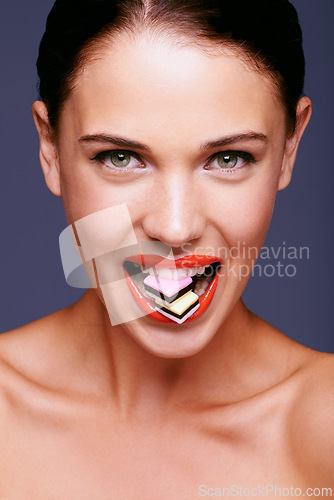 Image of Beauty, lipstick and woman in portrait with candy in mouth, makeup and creativity with shiny cosmetic product. Licorice, sweets and orange lip gloss for aesthetic with art on purple background