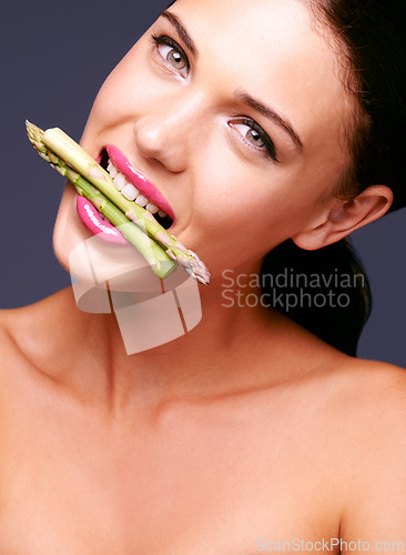 Image of Woman, lipstick and vegetables in mouth in portrait, beauty and nutrition for vegan cosmetic product in studio. Cruelty free makeup, cosmetology and asparagus with pink lip gloss on grey background