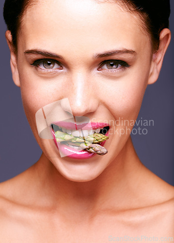 Image of Woman face, lipstick and vegetable in mouth for beauty, nutrition and vegan cosmetic product. Cruelty free makeup, portrait and asparagus with pink lip gloss for aesthetic on purple background