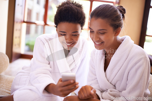 Image of Beauty, phone and spa with woman friends in robes for luxury pampering or treatment together. Smile, app and social media with happy young people at resort or salon for wellness or weekend getaway