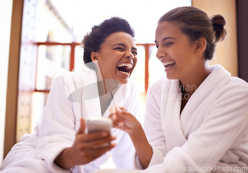 Image of Beauty, phone and spa with women laughing in robes for luxury pampering or treatment together. Happy, app and social media with funny young friends at resort or salon for wellness or weekend getaway