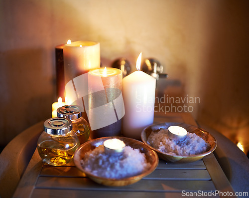 Image of Spa, candle and oil with salt in room for peace or luxury with aromatherapy to relax, zen and meditation. Aromatic or cosmetic liquid, table and candlelight for mindfulness or wellness and self care.