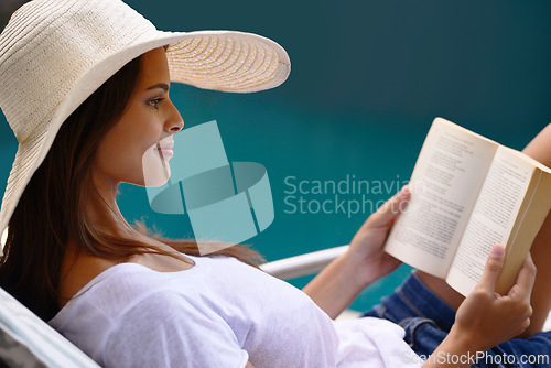 Image of Holiday, reading and woman at pool with book, hat and relax with happy summer travel on hotel patio. Vacation, deck chair and girl with smile, lounge and story with sunshine, weekend or luxury resort