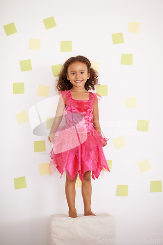 Image of Child, girl and smile with standing against wall with sticky notes, ottoman and excited with creativity. Kid, female person and happy with playing for development, growth and cute in pink dress