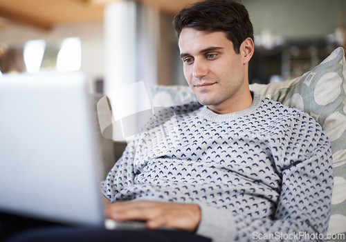 Image of Man, living room and sofa with typing on laptop for remote work as freelance journalist for newspaper and online research. Male person, home and focus on internet to search on information for article