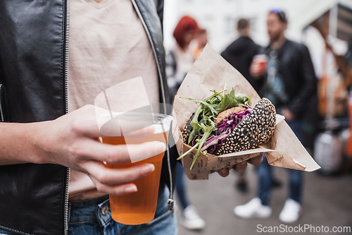 Image of Close up of woman hands holding delicious organic salmon vegetarian burger and homebrewed IPA beer on open air beer an burger urban street food festival in Ljubljana, Slovenia.