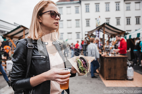 Image of Close up of woman hands holding delicious organic salmon vegetarian burger and homebrewed IPA beer on open air beer an burger urban street food festival in Ljubljana, Slovenia.