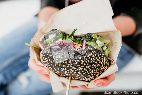 Image of Close up of woman hands holding delicious organic salmon vegetarian burger on open air beer an burger urban street food festival in Ljubljana, Slovenia.
