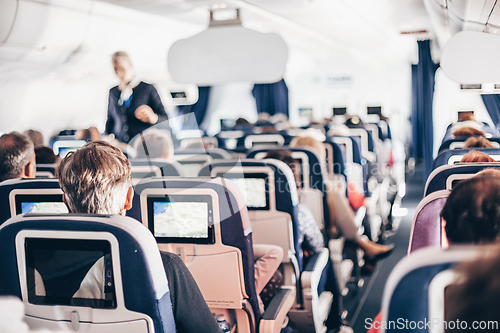 Image of Interior of airplane with passengers on seats and stewardess in uniform walking the aisle, serving people. Commercial economy flight service concept.