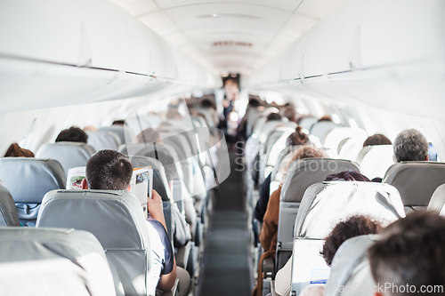 Image of Interior of airplane with passengers on seats and stewardess in uniform walking the aisle, serving people. Commercial economy flight service concept.