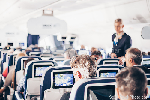 Image of Interior of airplane with passengers on seats and stewardess in uniform walking the aisle, serving people. Commercial economy flight service concept.