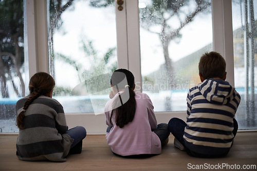 Image of Rain, window and sad child on a floor unhappy, upset or annoyed by bad weather at home. Glass, disappointed and sibling kids in a living room frustrated by storm, cold or unexpected winter disaster