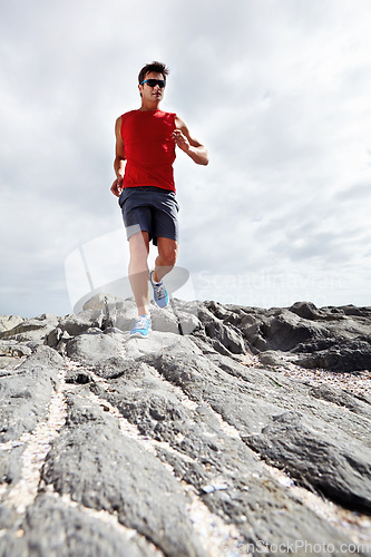 Image of Male runner, rocky terrain and training, exercising outdoors and seaside for marathon. Fitness, sports and sunglasses for active endurance athlete, health and cardio heart wellness for dedicated man