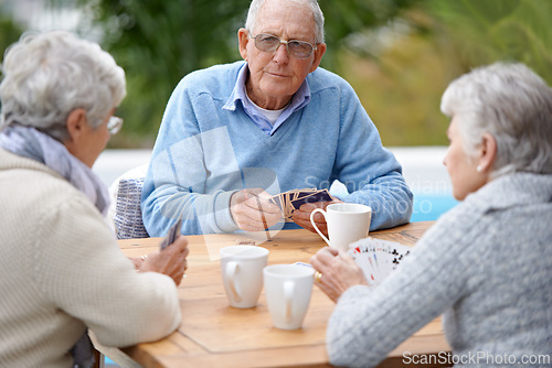 Image of Poker, playing cards and senior group in retirement, outdoor and relaxed in garden, backyard and terrace. Elderly people, bridge and smile with coffee, table and outside for relaxation, fun and games