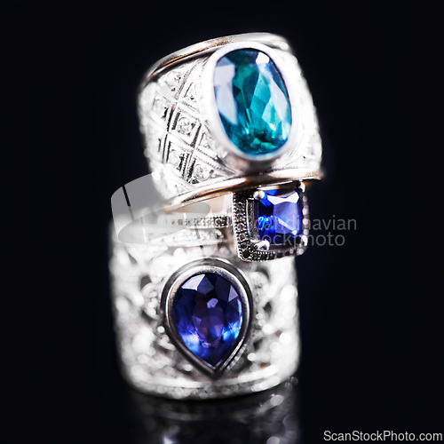 Image of Gemstone, silver and rings on a black background of luxury or expensive present for engagement or marriage in studio. Jewelry, diamonds and blue or sapphire rock in closeup, stack and rich accessory