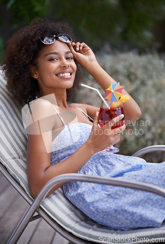 Image of African, woman and sunbathing with cocktail for summer on vacation, tropical drink and sunglasses for time fun. Happy, smile or female person laying on resort deck, comfortable or wellness or liquid