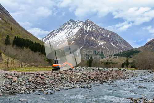 Image of Majestic mountain backdrop behind an excavator at riverbank duri