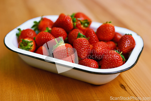 Image of Fruit, health and strawberry bowl in kitchen of home, on wooden counter top for diet or nutrition. Food, wellness and lose weight with berries on surface in apartment for detox, minerals or vitamins