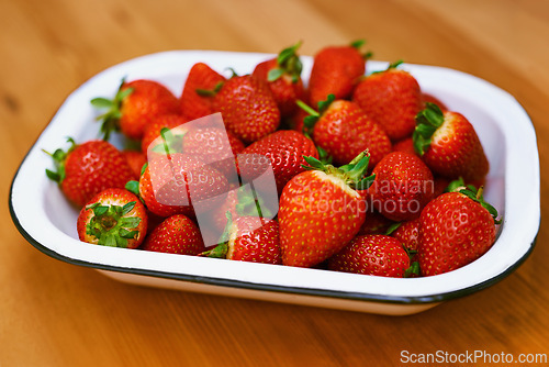 Image of Fruit, food and strawberry bowl in kitchen of home, on wooden counter top for diet or nutrition. Health, wellness and lose weight with berries on surface in apartment for detox, minerals or vitamins