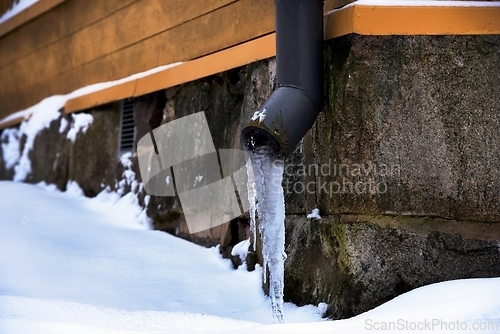Image of icy drainpipe near the stone foundation of an old house
