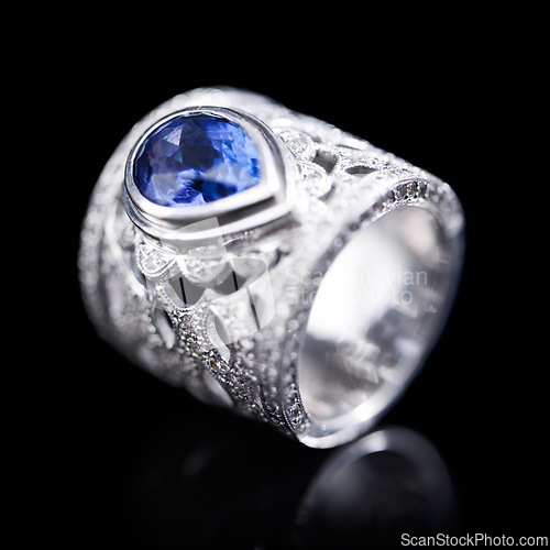 Image of Gemstone, silver and ring on a black background of luxury or expensive present for engagement or marriage in studio. Jewelry, diamonds and blue or sapphire rock in closeup, reflection and accessory