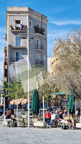 Image of BARCELONA, SPAIN - APRILL 2, 2024: Group of people sitting at tables in front of a tall building