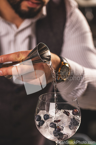 Image of Bartender pouring gin into glass with ice and berries