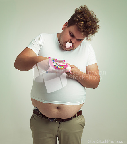 Image of Obesity, weight gain and comic for man in studio with marshmallow for unhealthy eating, sugar and candy. Overweight person with hand in sweet packet and fat stomach for greed, comedy and humor indoor