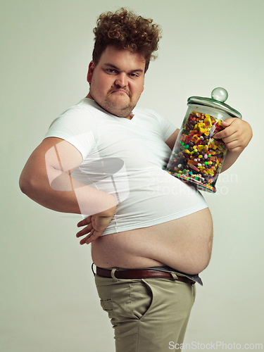 Image of Candy, jar and portrait of silly man in studio for snacks, sweets and dessert in container. Comic, goofy and overweight, isolated and plus size person with glass for unhealthy diet on background