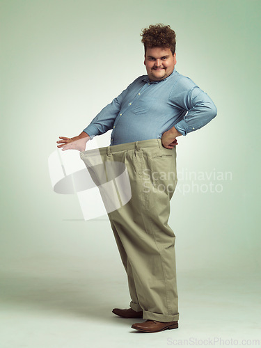 Image of Happy man, portrait and plus size with weight loss or pants for measurement or waist on a studio background. Male person with smile for healthy diet, obesity or overweight in clothing on mockup space