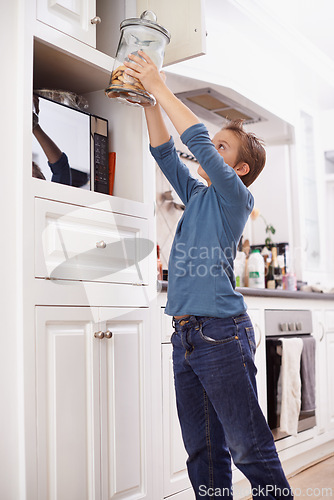 Image of Cookies, jar and child in kitchen of home with glass, container or sneaky snack on sweets. House, cupboard and kid craving a taste of sugar with addiction to unhealthy food and reach for biscuit