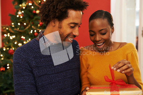 Image of Christmas, present and black couple giving a box or opening surprise on festive holiday or vacation with happiness. Excited, woman and man offer a gift in home with love and kindness in marriage