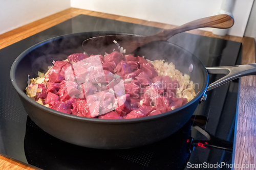 Image of sliced onions and meat are frying in a pan