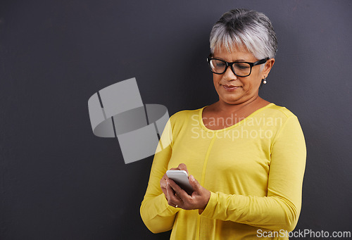 Image of Glasses, phone and senior woman in studio reading text message, email or blog on internet. Spectacles, technology and elderly female person learning to network on cellphone by black background.