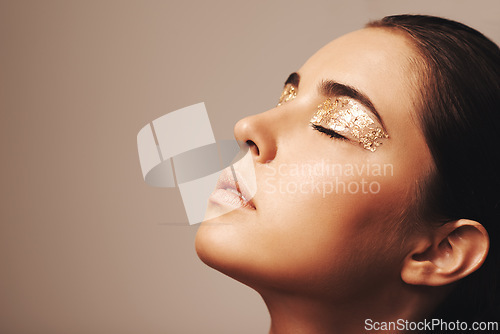 Image of Woman, face and gold glitter on eyes for beauty, cosmetology and glamour with cosmetics on beige background. Eyeshadow, makeup and fashion model in studio, art or creativity with shimmer and glow