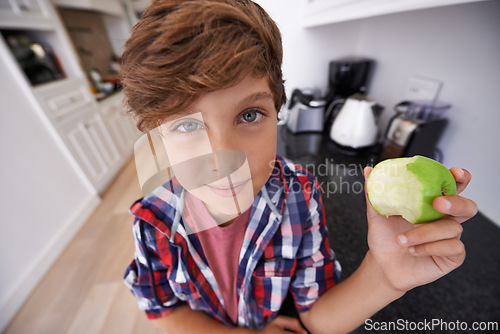 Image of Portrait, apple and children with boy in kitchen of home for health, organic diet or nutrition. Face, fruit and confident young teen kid eating green food in apartment for growth or development